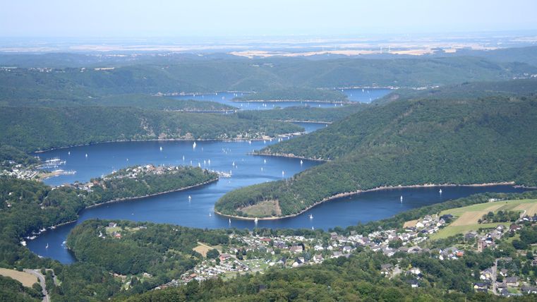 A picturesque view of a river with many coves and small boats. Surrounded by gentle hills and green riverside land.