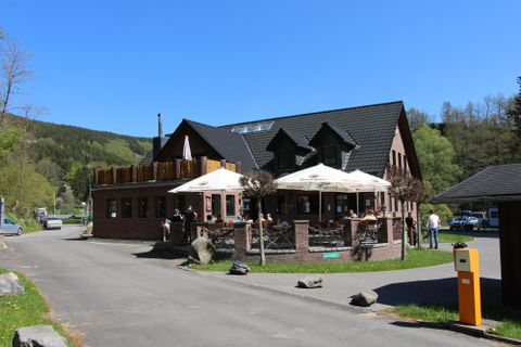 Ein charmantes Restaurant mit einer Terrasse und Sonnenschirmen. Es liegt in einer ruhigen Umgebung, umgeben von Bäumen.
