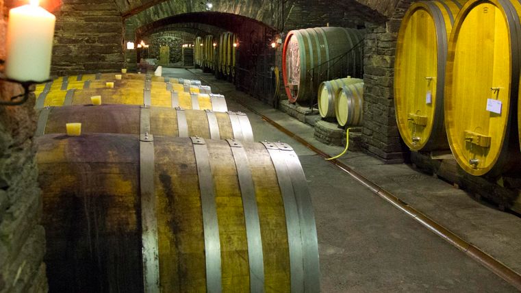 Een wijnkelder met grote houten vaten en zachte verlichting van kaarsen. De sfeer is rustiek en uitnodigend.