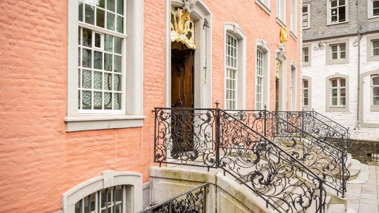 Een elegant gebouw met een roze gevel en historische ramen. De smeedijzeren leuningen leiden naar de voordeur.