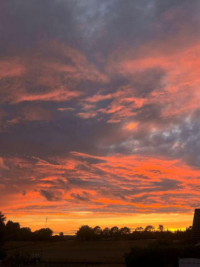 A beautiful sunset with bright orange and pink clouds. The landscape in the foreground is silhouetted and offers a peaceful view.