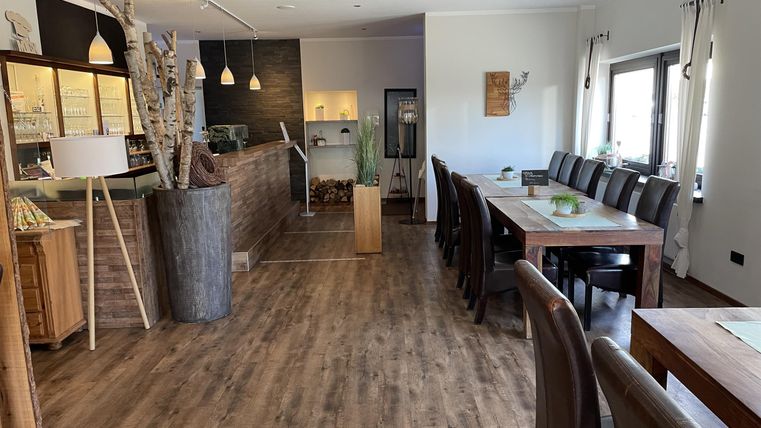 Een modern restaurant met een houten vloer en grote ramen. Tafels zijn gedekt voor gasten en een uitnodigende sfeer is zichtbaar.