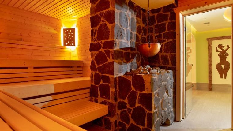 A modern sauna with wooden benches and a stone stove. The room is warmly lit and radiates a relaxing atmosphere.