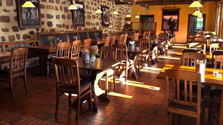 Ein gemütliches Restaurant mit Holzstühlen und -tischen. Sonnenlicht strömt durch die Fenster und beleuchtet den Raum.