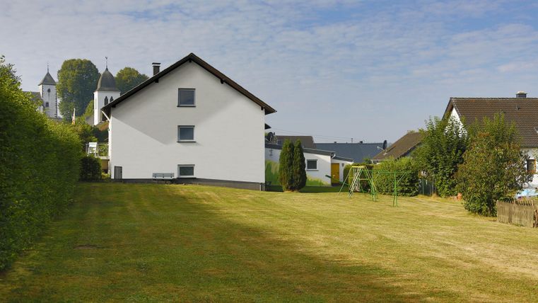 Ein ruhiger Garten mit einem gepflegten Rasen und einem weißen Haus. Im Hintergrund sind weitere Häuser und Bäume zu sehen.