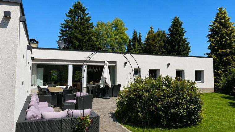 Ein modernes Haus mit einem schönen Außenbereich. Grüne Rasenflächen und Sitzgelegenheiten laden zum Entspannen ein.