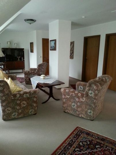 Ein einladendes Wohnzimmer mit zwei bequemen Sessel, einem Couchtisch und einem Teppich. Die Wände sind hell gestrichen und es gibt Türen zu anderen Räumen.