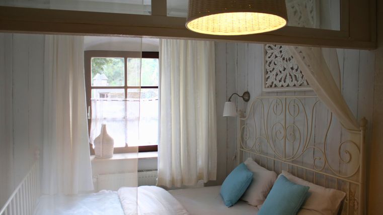 A bright bedroom with a white bed and blue pillows. Large windows let in plenty of light and give the room a cozy atmosphere.