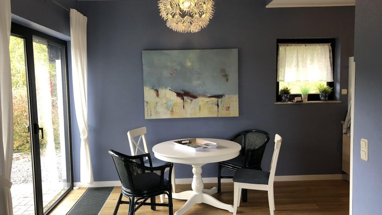 Een gezellige eetruimte met een ronde tafel en vier stoelen. De muren zijn in een mooie blauwtint geverfd, en een groot raam laat veel licht binnen.