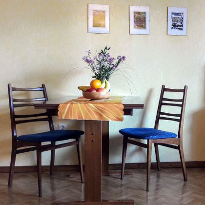 Een kleine tafel met twee stoelen is in de ruimte gedecoreerd. In het midden staat een fruitschaal met fruit en een vaas met bloemen.