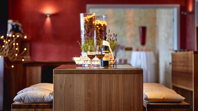 Ein stilvoller Innenraum mit einem hölzernen Tisch und gemütlichen Sitzgelegenheiten. Auf dem Tisch stehen Gläser und dekorative Elemente in einem warmen, einladenden Ambiente.