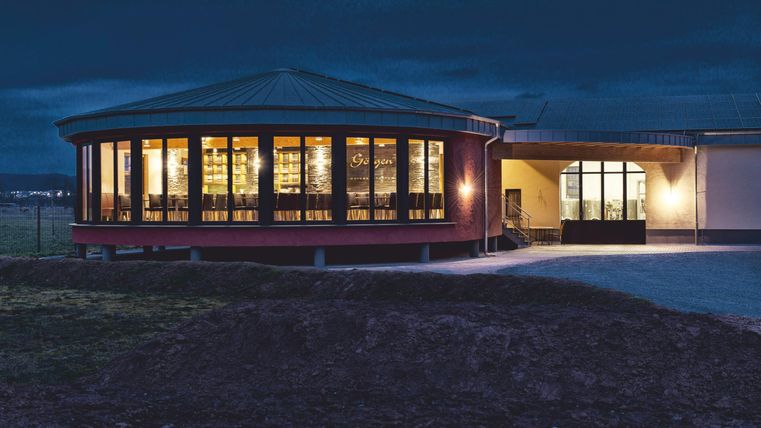 Een modern gebouw in ronde vorm, 's nachts verlicht. Het interieur lijkt uitnodigend en comfortabel te zijn.