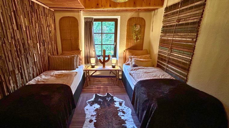 A cozy bedroom with two single beds and a wooden lamp picture. The walls are decorated with natural materials, and a window provides plenty of daylight.