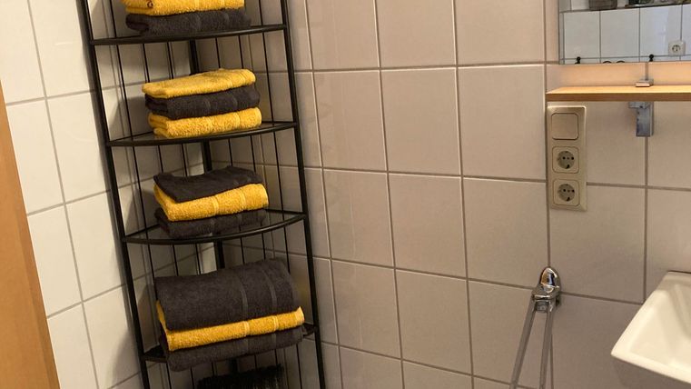 A bathroom with white tiles and a towel rack. The rack is filled with yellow and gray towels.