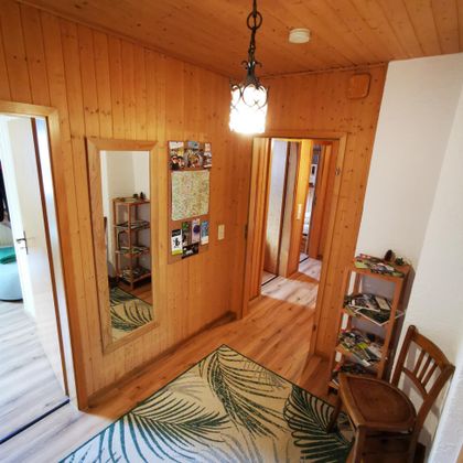 Een gezellige gang met houten bekleding en een grote spiegel. Links staat een stoel en rechts bevindt zich een kast met tijdschriften.