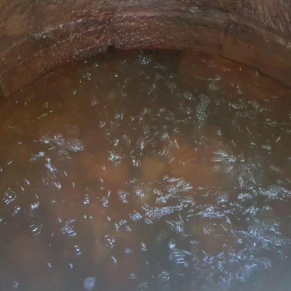 Ein Brunnen mit braunem Wasser, das sprudelt. Die Innenwände sind aus Ziegeln.
