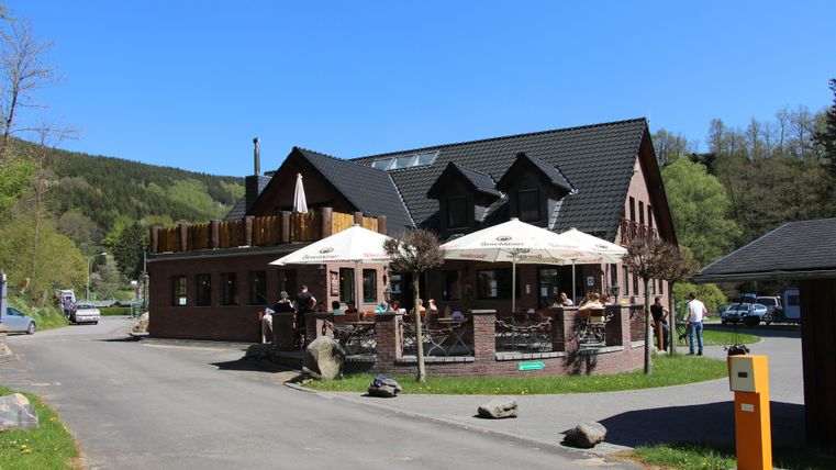 Ein charmantes Restaurant mit einer Terrasse und Sonnenschirmen. Es liegt in einer ruhigen Umgebung, umgeben von Bäumen.