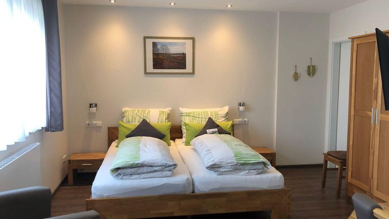 Ein gemütliches Schlafzimmer mit zwei Betten, die mit grünen Kissen und Decken dekoriert sind. Der Raum ist hell und modern eingerichtet, mit einem Fenster und einem Wandbild.