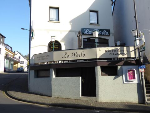 Ein Restaurant mit dem Namen "La Perla" an einer Straßenecke. Die Fassade zeigt eine moderne Gestaltung mit einem einladenden Außenbereich.