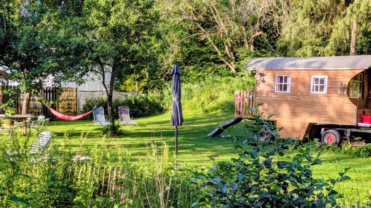 A cozy garden with a wooden cabin and a hammock. The surroundings are green and inviting, ideal for relaxing.