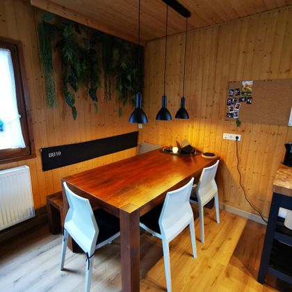 Een stijlvolle eettafel van hout met witte stoelen in een gezellige ruimte. Groene planten en warm licht zorgen voor een uitnodigende sfeer.