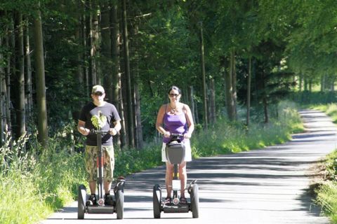 Twee personen rijden op Segways langs een bospad. De omgeving is groen en zonnig.