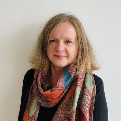 Eine Frau mit lockigem Haar trägt einen farbenfrohen Schal. Sie lächelt vor einem hellen Hintergrund.