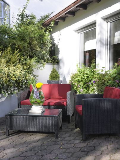 Eine gemütliche Sitzecke im Freien mit roten und schwarzen Möbeln. Grüne Pflanzen und Blumen verleihen dem Platz eine einladende Atmosphäre.