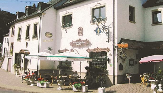 Een gezellig gasthuis met een uitnodigend terras en bloeiende planten. De gevel is versierd met decoratieve elementen.
