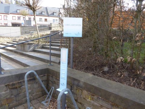 Eine Fahrradbastelstation mit einem kleinen Schild und Werkzeug. Im Hintergrund sind Häuser und eine Treppe zu sehen.