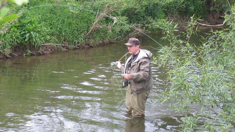 Man stands in the Kyll with a fishing rod in hand
