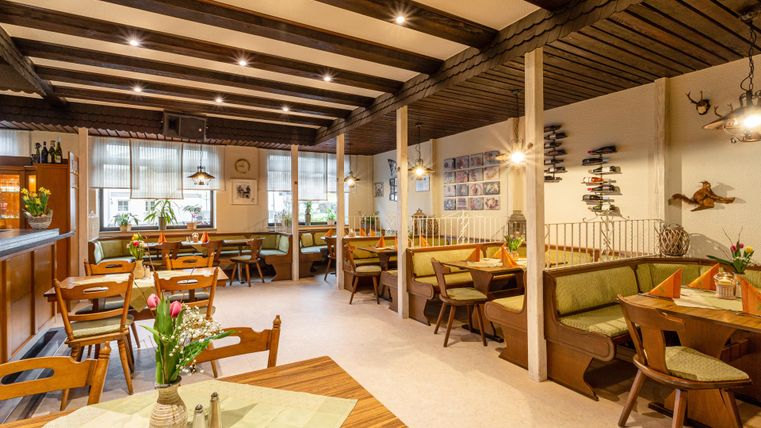 Een gezellig restaurant met houten plafonds en groen gestoffeerde banken. De inrichting is uitnodigend en vriendelijk.