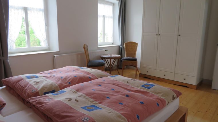 Ein gemütliches Schlafzimmer mit zwei Betten und bunten Bettdecken. Es gibt einen Schreibtisch, einen Stuhl und einen Kleiderschrank.