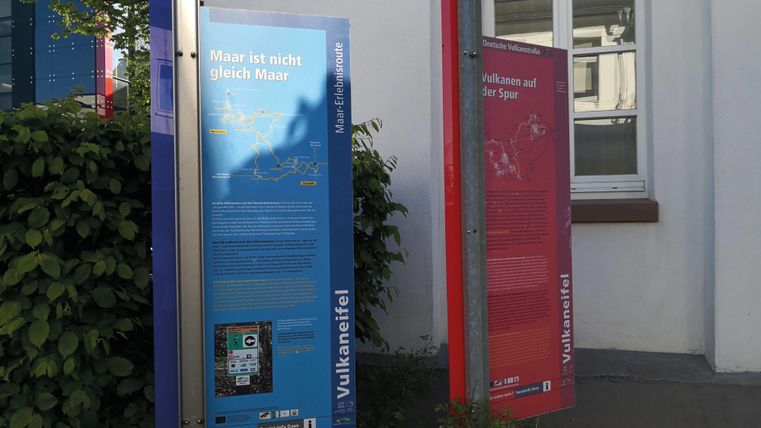 Zwei Infotafeln stehen an einer Wand. Die Tafeln informieren über Meere und Vulkane.