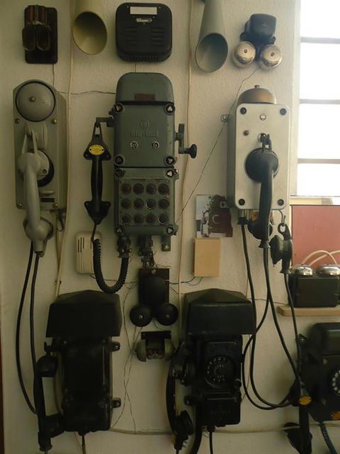 Verschiedene historische Telefone und Kommunikationsgeräte sind an einer Museumswand ausgestellt. Sie zeigen die Entwicklung der Telefontechnik.