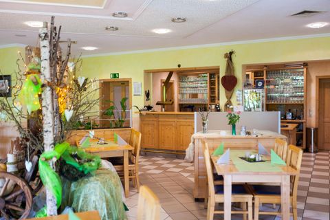 An inviting restaurant with wooden tables and a bright, friendly atmosphere. Plants and decorations create a cozy ambiance.