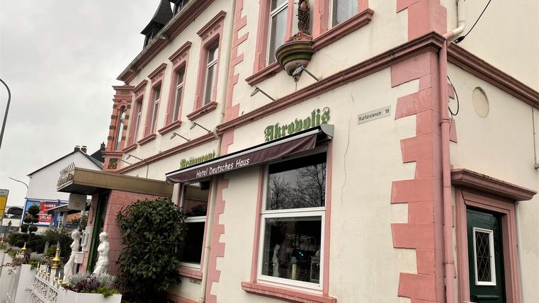 Een wit-roze gebouw met een uitnodigende entree. Het is een restaurant met een verzorgde buitenruimte.