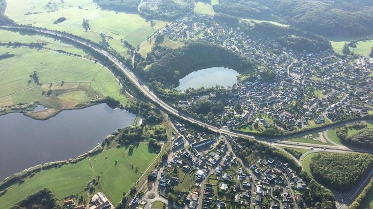 Een luchtfoto van een schilderachtig landschap met meerdere kleine meren en een stad. De omgeving bestaat uit groene velden en heuvels.