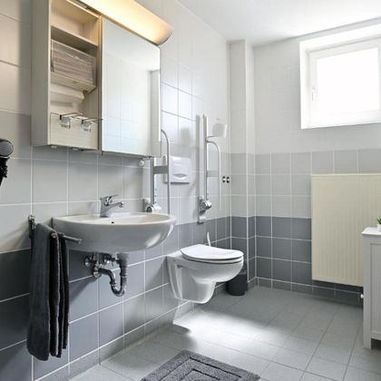 A modern bathroom with gray tiles and light walls. There is a sink, a toilet, and a large mirror.