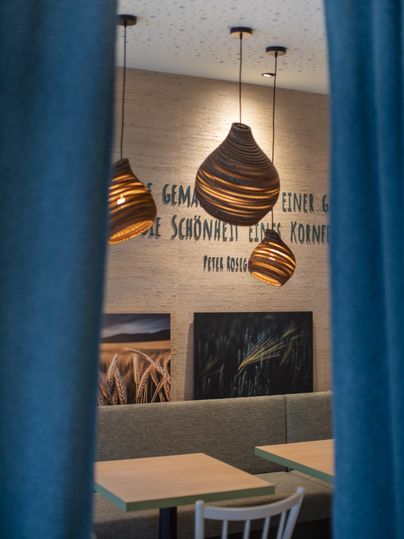 Een gezellige ruimte met houten hanglampen en een neutrale wandkleur. Tafels en stoelen nodigen uit om te blijven zitten.