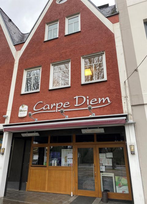 Ein rotes Gebäude mit einem Eingang aus Holz. Über dem Eingang steht "Carpe Diem".