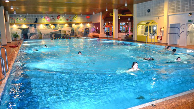 Ein Innenpool mit klarem Wasser und mehreren Schwimmern. Die Wände sind bunt gestaltet und schaffen eine einladende Atmosphäre.