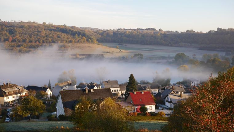 A tranquil landscape with a village in the morning mist. Gentle hills and green meadows surround the buildings.