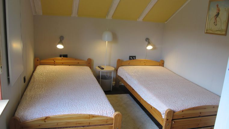Ein gemütliches Schlafzimmer mit zwei Einzelbetten aus Holz. Die Wände sind hell gestrichen und eine Stehlampe sorgt für zusätzliches Licht.