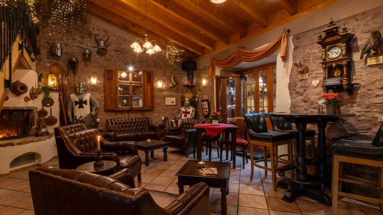 Eine gemütliches Restaurant mit Leder-Sesseln und Holzdecke. An den Wänden hängen Dekorationen und eine alte Uhr, während ein Fenster Licht in den Raum lässt.