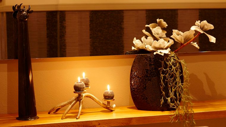 A stylish room with a long wooden table surface, decorated with flowers and candles. In the background, decorative animal heads can be seen on the wall.