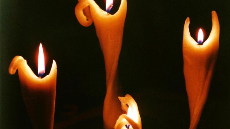 Drei brennende Kerzen mit geschwungener Form stehen im Dunkeln. Das warme Licht schafft eine gemütliche Atmosphäre.