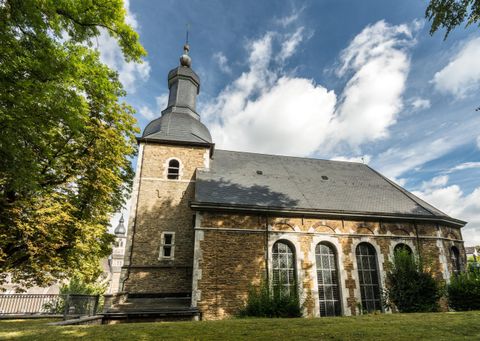 A charming church with a black roof and a distinctive tower.
Surrounded by trees and a clear sky.