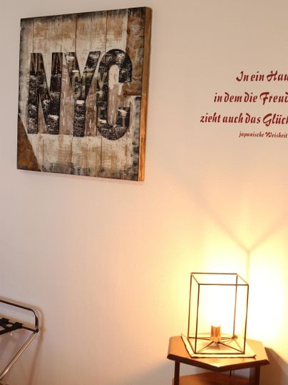 Ein buntes Wandbild mit der Aufschrift "NYC" hängt an der Wand. Neben dem Bild steht eine dekorative Lampe auf einem Tisch.
