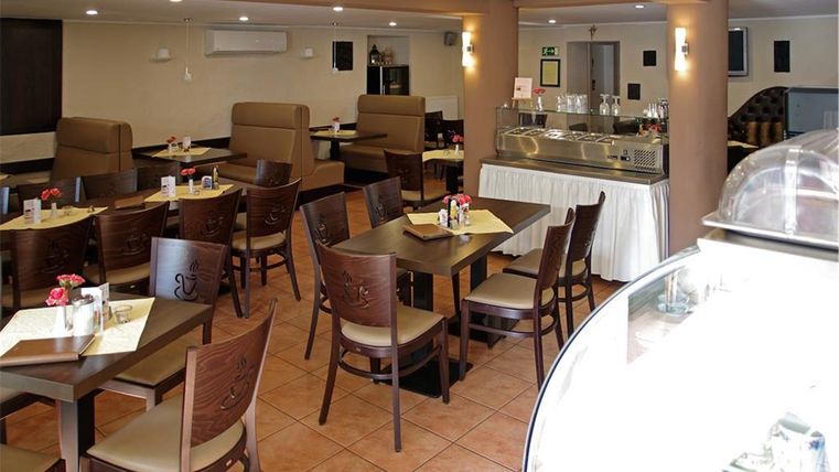 Ein gemütliches Restaurant mit Holzstühlen und Tischen. Es gibt eine Tafel und eine Kuchenauslage auf der rechten Seite.